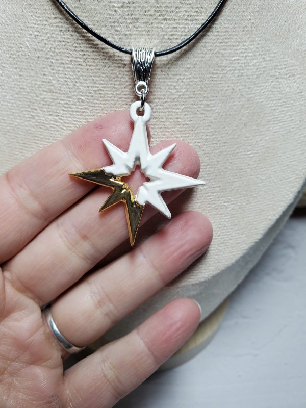 Pendentif en céramique en forme d'étoile, avec des accents dorés élégants et une finition brillante, parfait pour ajouter une touche lumineuse et sophistiquée.