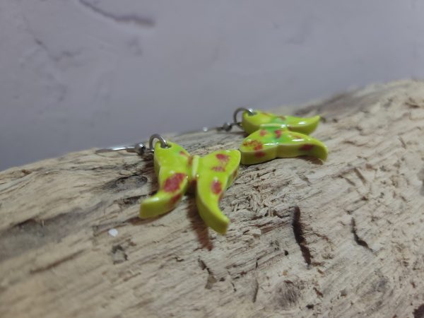Élégantes boucles d'oreilles en céramique façonnées en forme de papillon, avec des détails délicats et une finition brillante qui reflète la lumière avec douceur.