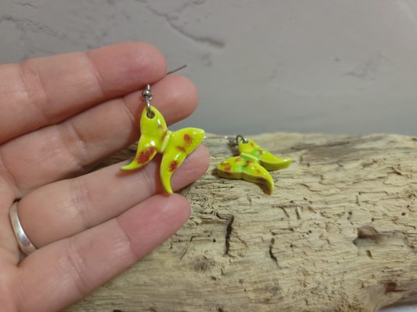 Élégantes boucles d'oreilles en céramique façonnées en forme de papillon, avec des détails délicats et une finition brillante qui reflète la lumière avec douceur.