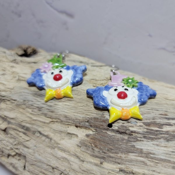 Boucles d’oreilles artisanales en céramique représentant une tête de clown souriant, aux couleurs vives et au style fantaisiste.