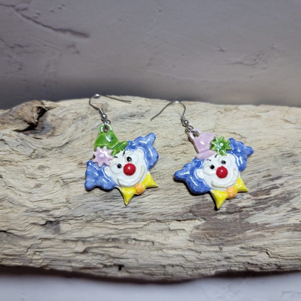 Boucles d’oreilles artisanales en céramique représentant une tête de clown souriant, aux couleurs vives et au style fantaisiste.