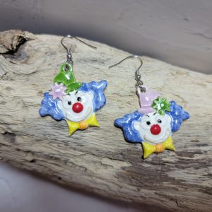 Boucles d’oreilles artisanales en céramique représentant une tête de clown souriant, aux couleurs vives et au style fantaisiste.